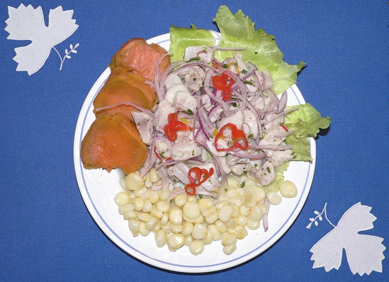 A plate of Peruvian ceviche with red onion, sweet potato and corn
