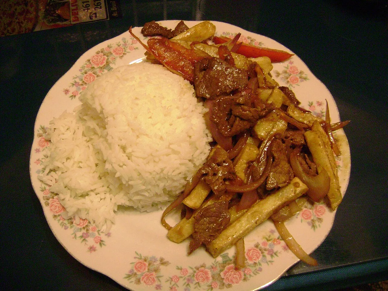 A plate of lomo saltado — stir-fried beef with onions, tomato and chips over rice